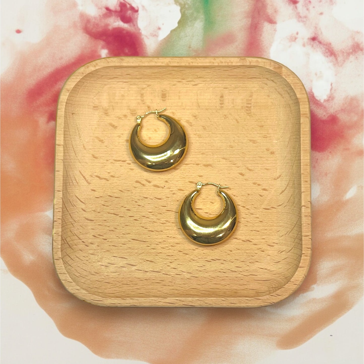 Glossy gold hoop earrings on a wooden tray, showcasing a minimalist, smooth finish perfect for versatile day-to-night styling.
