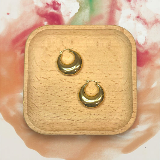 Glossy gold hoop earrings on a wooden tray, showcasing a minimalist, smooth finish perfect for versatile day-to-night styling.