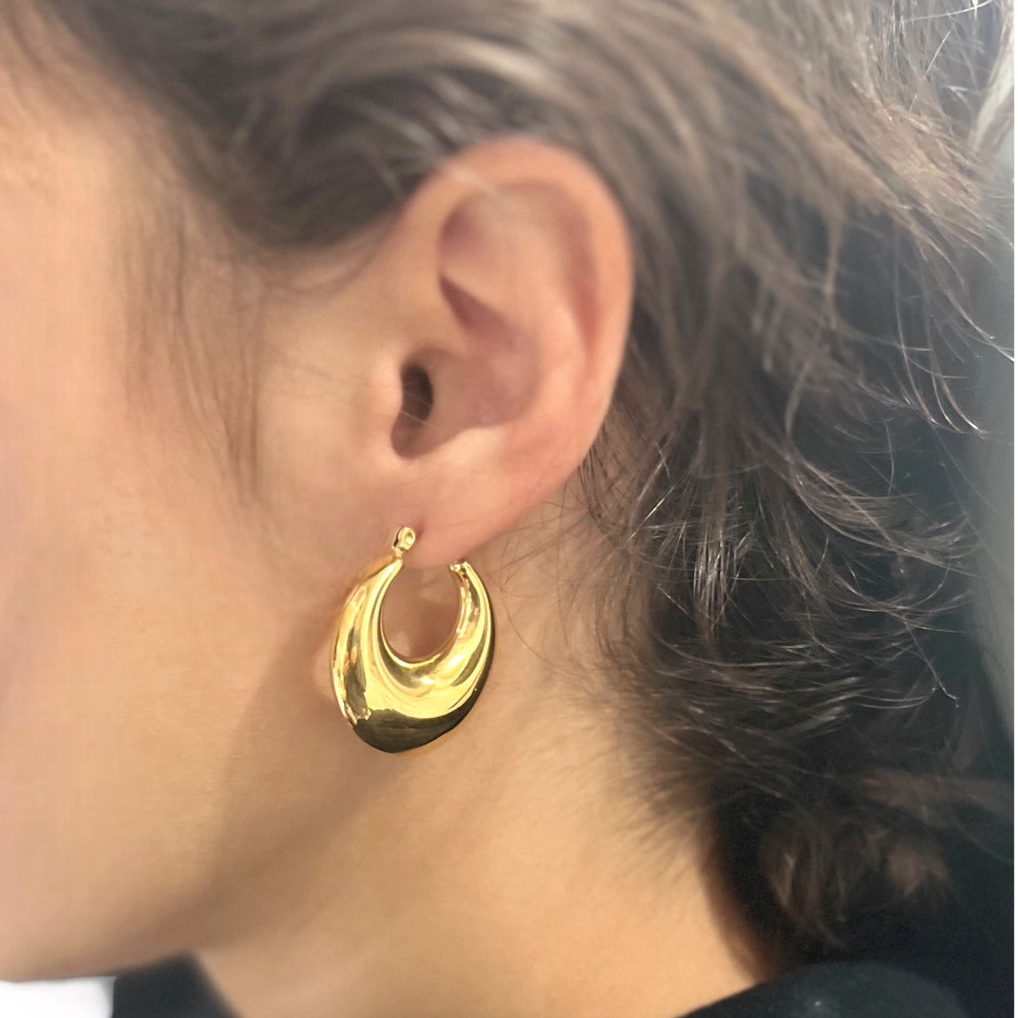 Close-up view of gold hoop earrings worn on an ear, highlighting their sleek, modern design and lightweight comfort. 