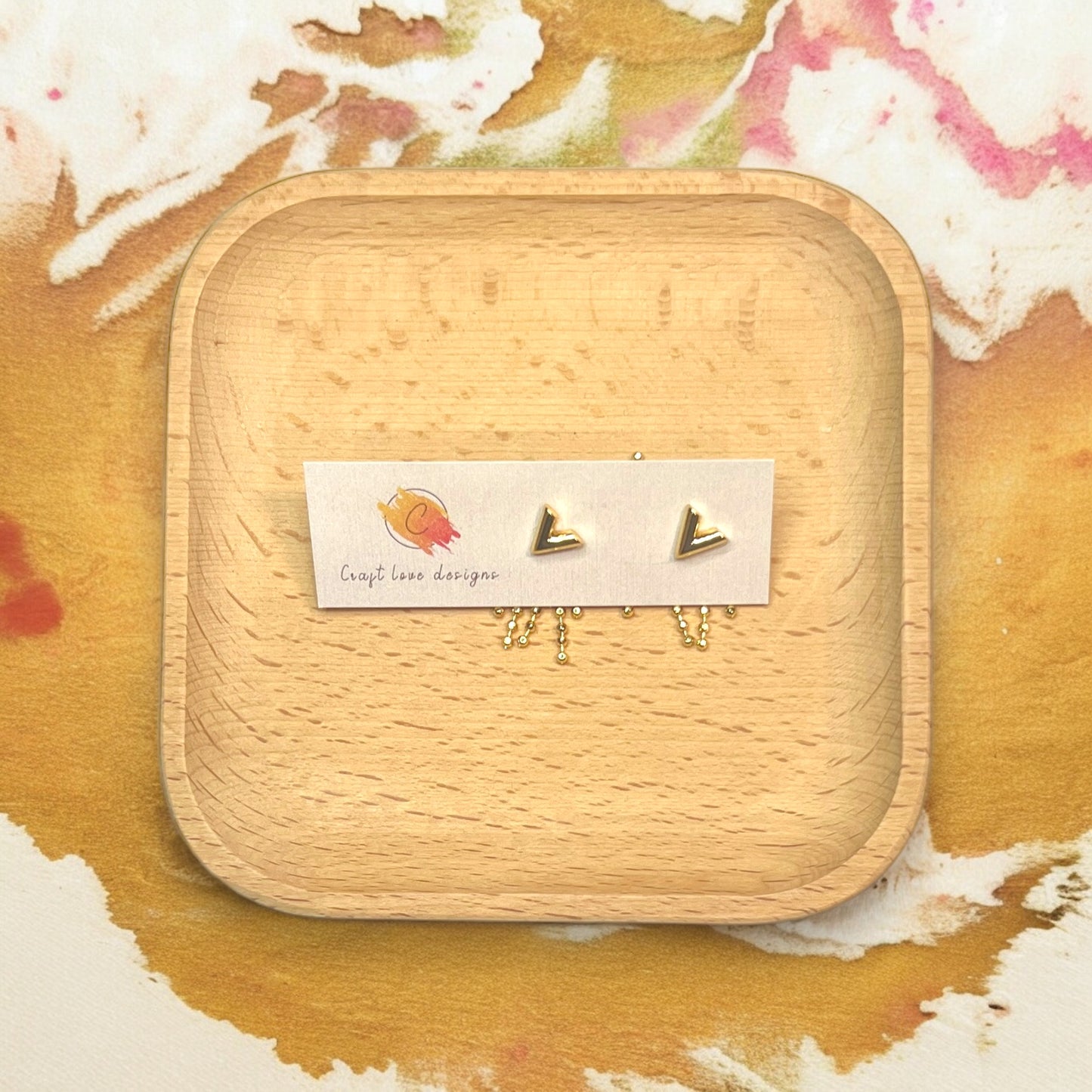 Gold V tassel earrings displayed on a wooden tray, highlighting sleek design with dangling gold beads for an elegant look.