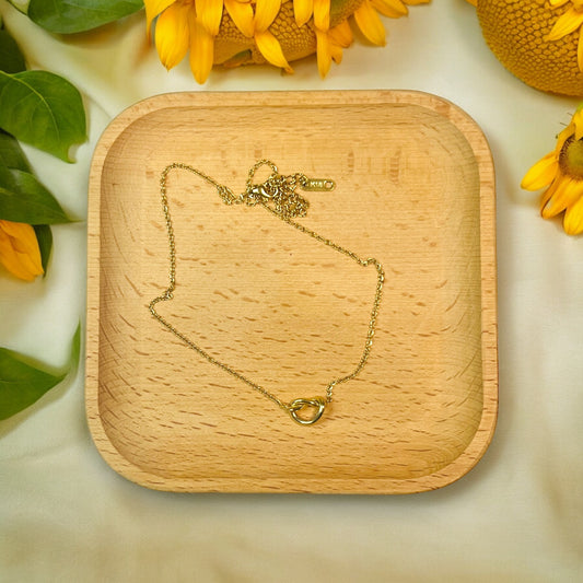  Minimal gold knot pendant necklace placed on a wooden tray, surrounded by sunflowers. 