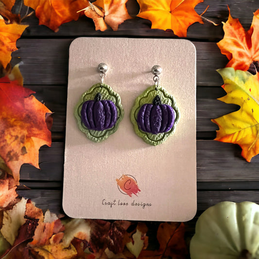 Green and purple pumpkin dangle earrings with a textured background featuring vibrant autumn leaves. Perfect for seasonal and festive wear.