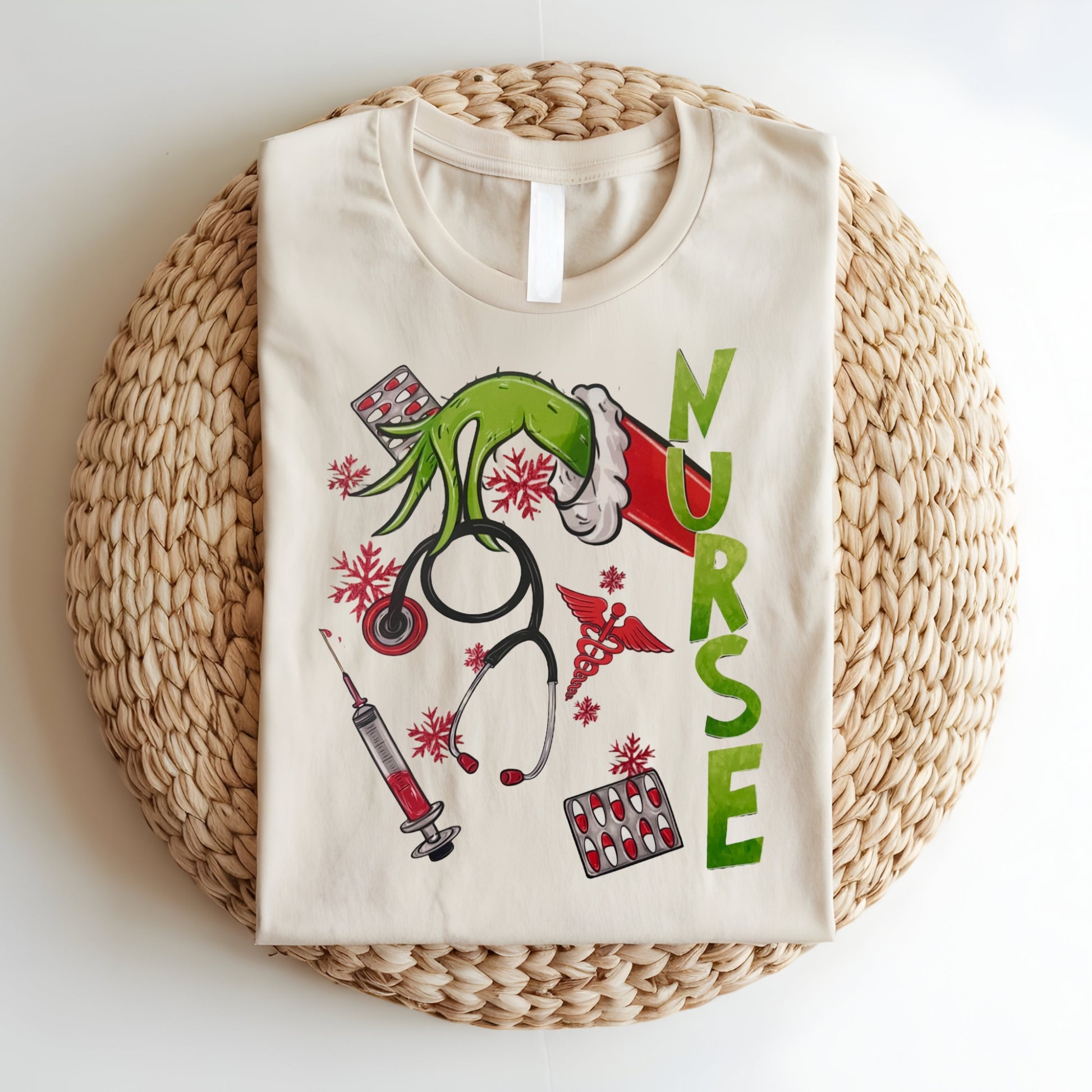 Flat lay of a beige Grinch-themed nurse t-shirt featuring holiday medical graphics like stethoscopes, syringes, and festive decor.
