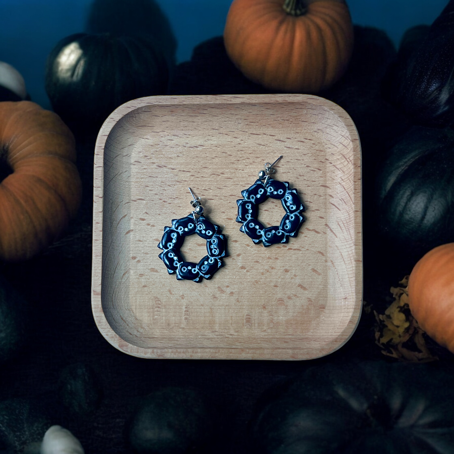Black cat wreath earrings showcased in a wooden tray with pumpkins and Halloween decor, perfect for fall-themed fashion.