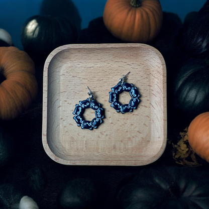 Black cat wreath earrings showcased in a wooden tray with pumpkins and Halloween decor, perfect for fall-themed fashion.