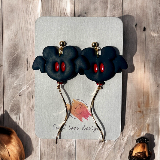 Black polymer clay bat earrings featuring red eyes and gold dangle accents, displayed on Craft Love Designs packaging.