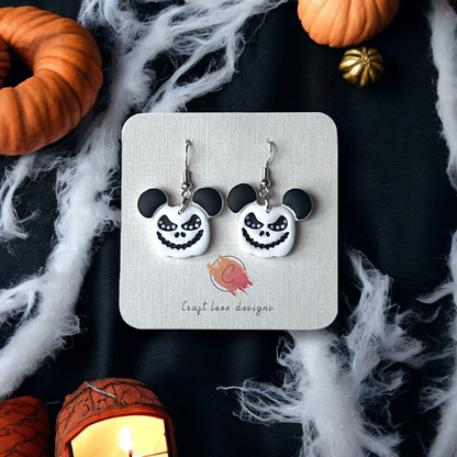 White and black Halloween earrings featuring Jack Skellington's face with Mickey Mouse ears, displayed on a card surrounded by pumpkins and cobwebs. 