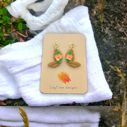 Latte and coral butterfly dangle earrings on a craft display, featuring soft floral accents and a nature-inspired design.