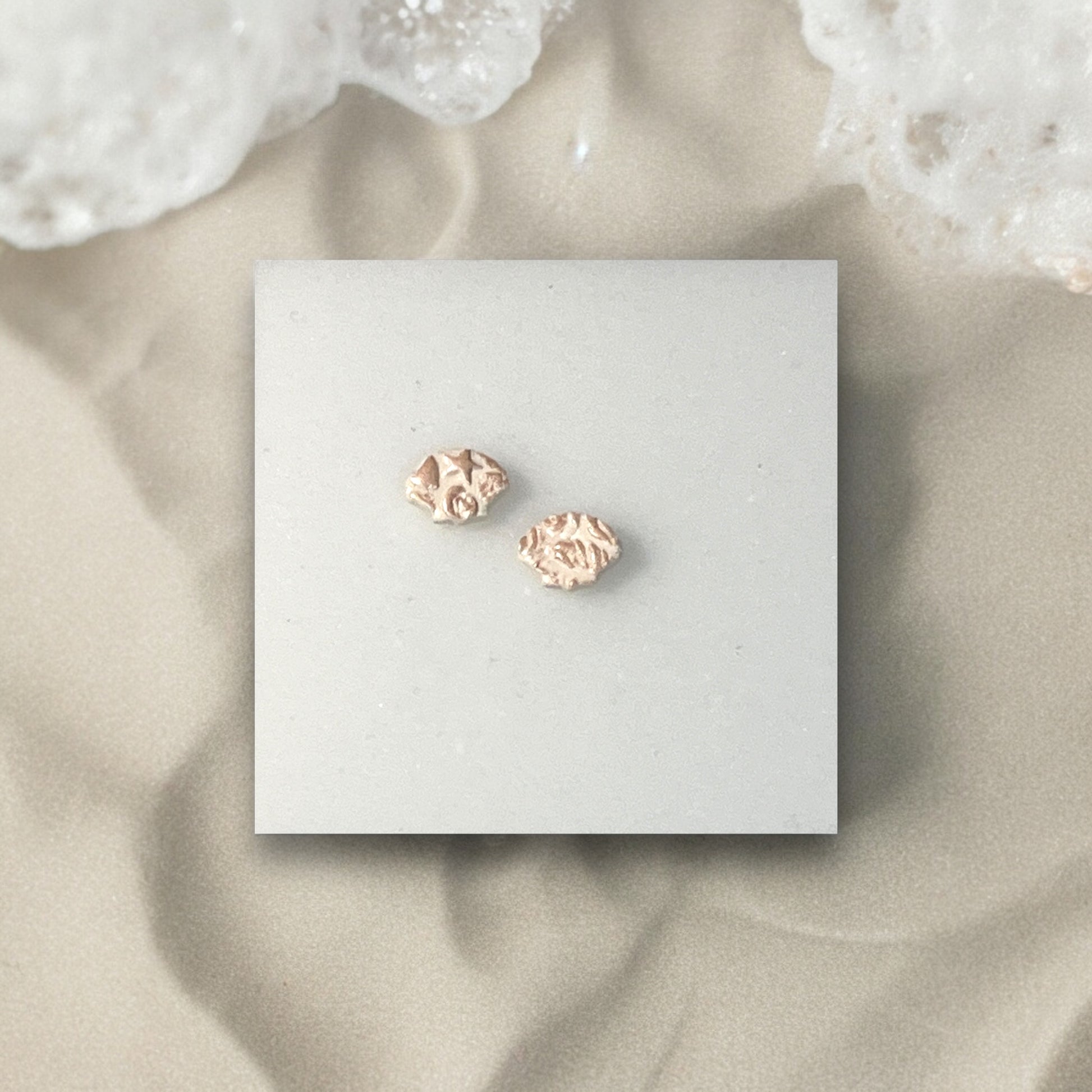Minimalist shot of textured earrings on a neutral background, highlighting the handcrafted design and soft sand-inspired texture.