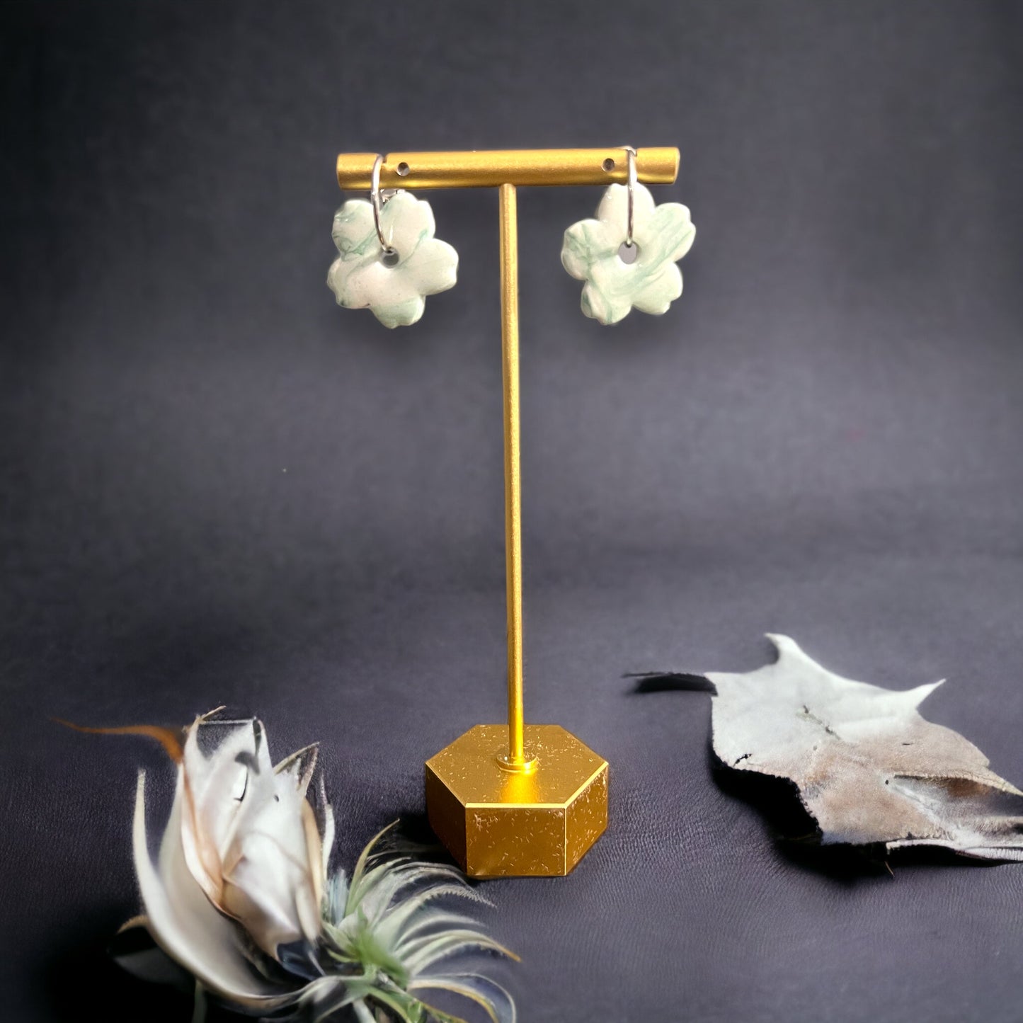 Close-up of mint green daisy-shaped hoop earrings hanging elegantly on a gold stand with minimalistic, nature-inspired decor.