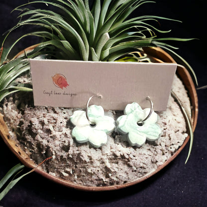 Mint green daisy hoop dangle earrings resting in a nature-themed background with air plants, giving off a fresh, floral vibe.