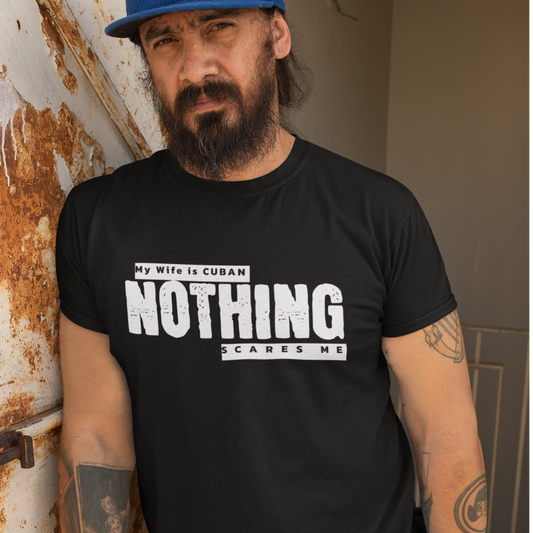  Man wearing a black "My Wife is Cuban, Nothing Scares Me" t-shirt, standing by a rustic background with a bold expression.