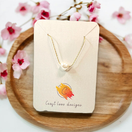 Close-up of a natural pearl necklace elegantly positioned on a display card with floral surroundings, highlighting its minimalistic beauty.