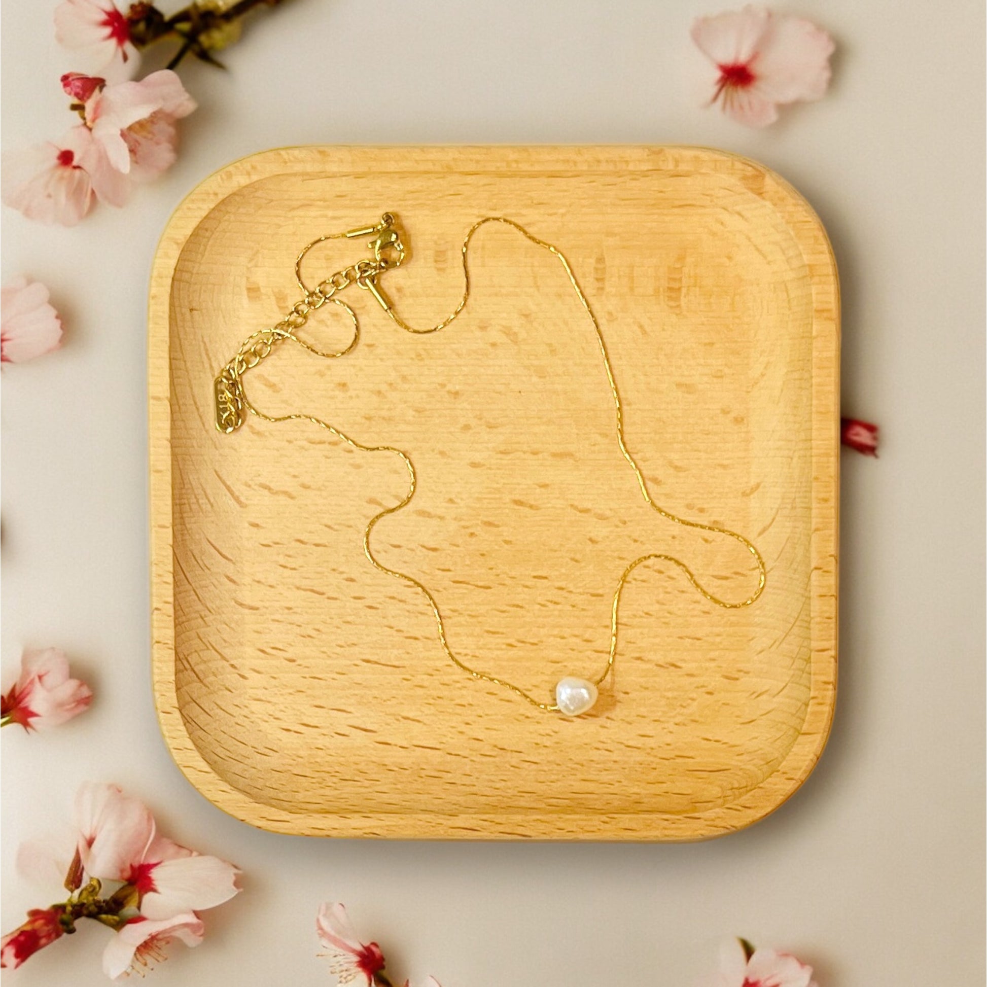 A delicate natural pearl necklace displayed on a wooden tray, showcasing its dainty gold chain and natural pearl centerpiece.
