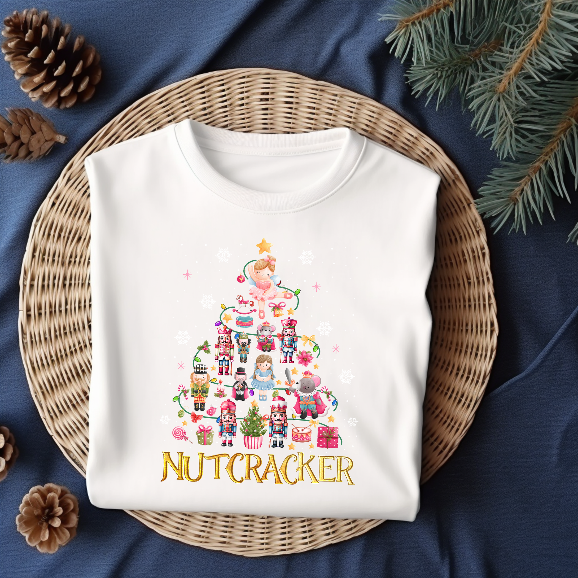 Flat lay of a white Nutcracker-themed Christmas t-shirt featuring festive characters like Clara, nutcrackers, and holiday decor.
