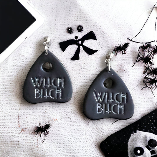 Black dangle earrings with a silver Ouija-inspired design and "Witch B***" text, spooky Halloween aesthetic. 
