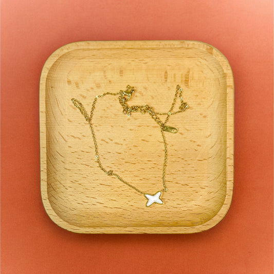 Gold necklace with petite X-shaped shell pendant, resting elegantly on a wooden tray, highlighting its minimalist, ocean-inspired design