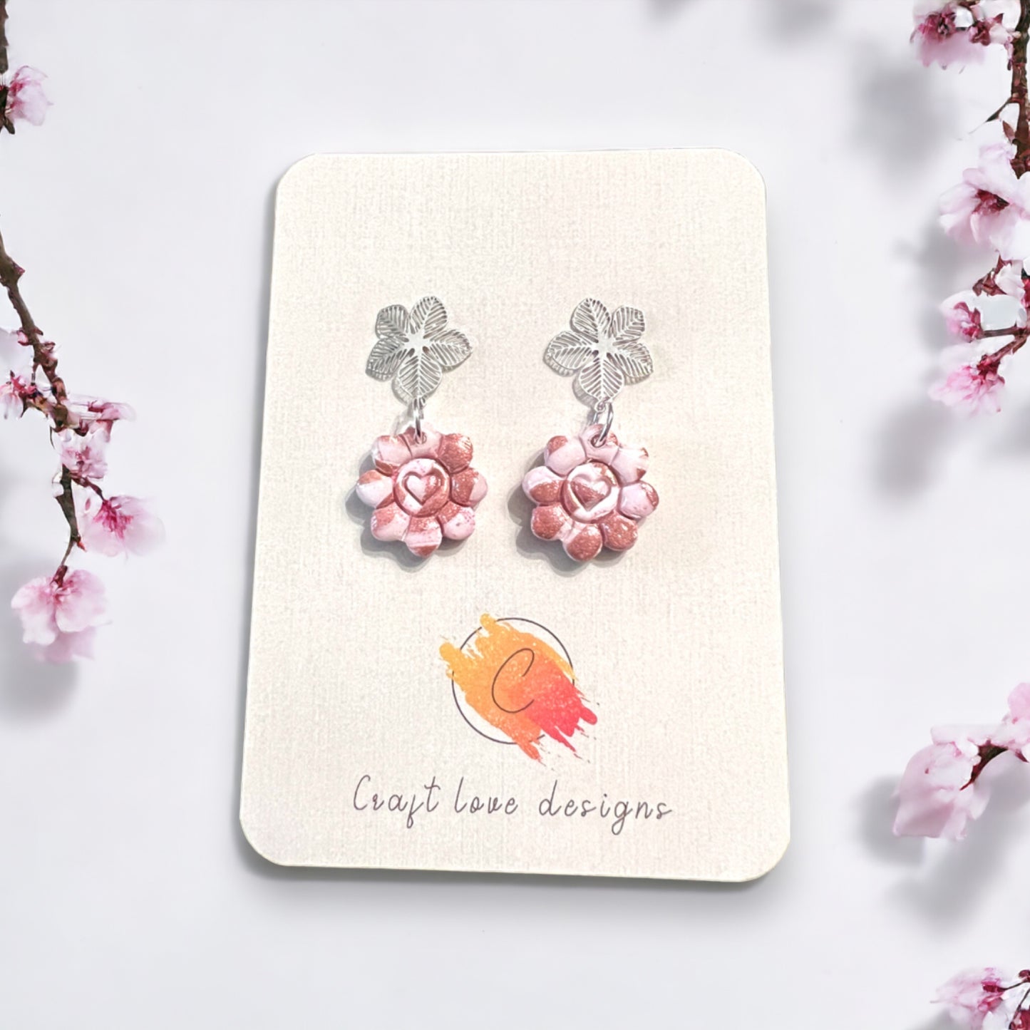 Elegant pinkish flower heart dangle earrings with silver floral tops, exuding a delicate and romantic charm. 