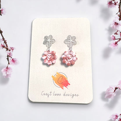 Elegant pinkish flower heart dangle earrings with silver floral tops, exuding a delicate and romantic charm. 