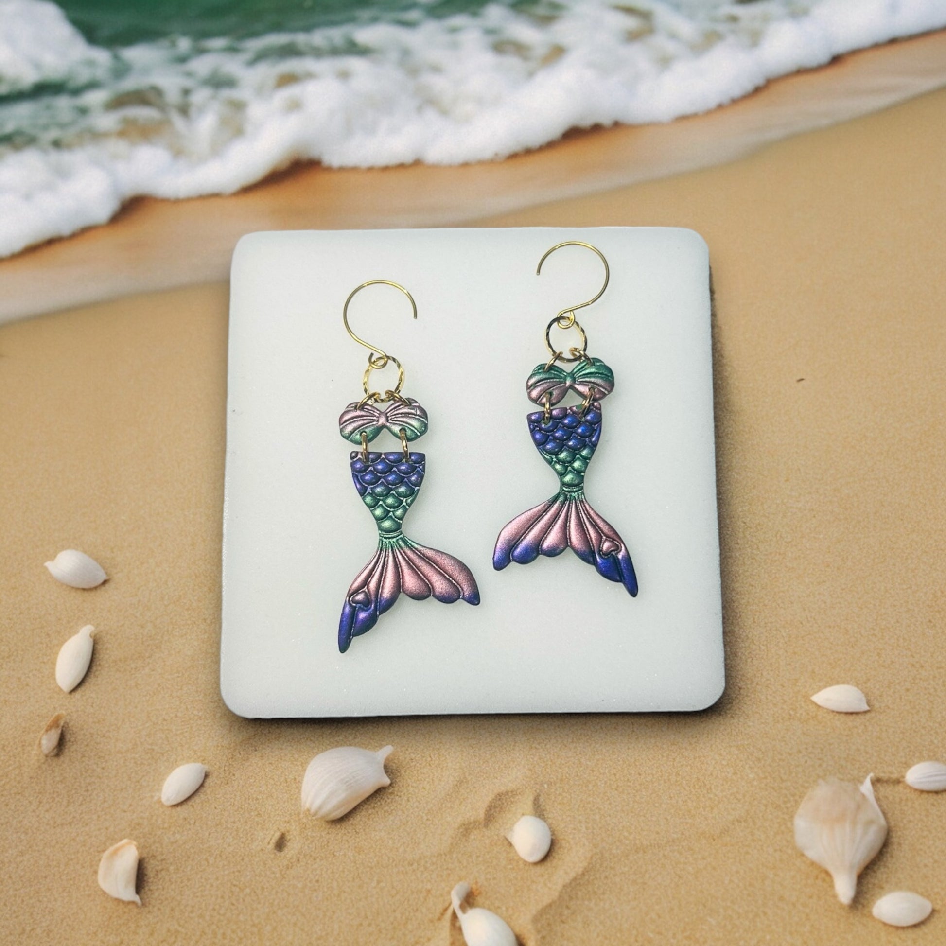  Pink flamingo earrings resting on a square decorative plate with a beach-themed backdrop. Perfect playful jewelry for summer outings.