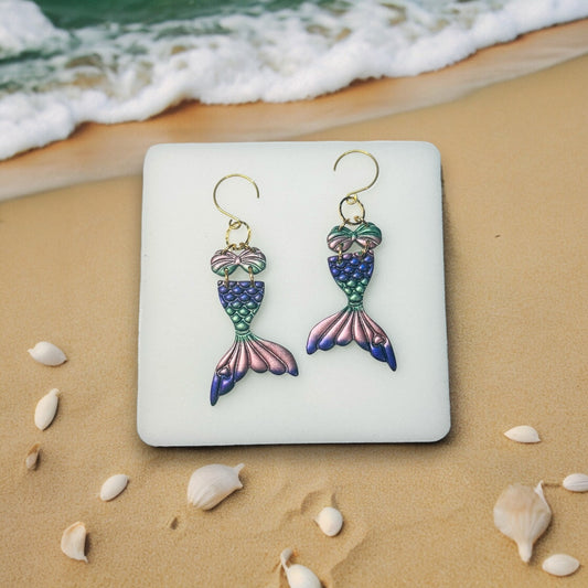  Pink flamingo earrings resting on a square decorative plate with a beach-themed backdrop. Perfect playful jewelry for summer outings.