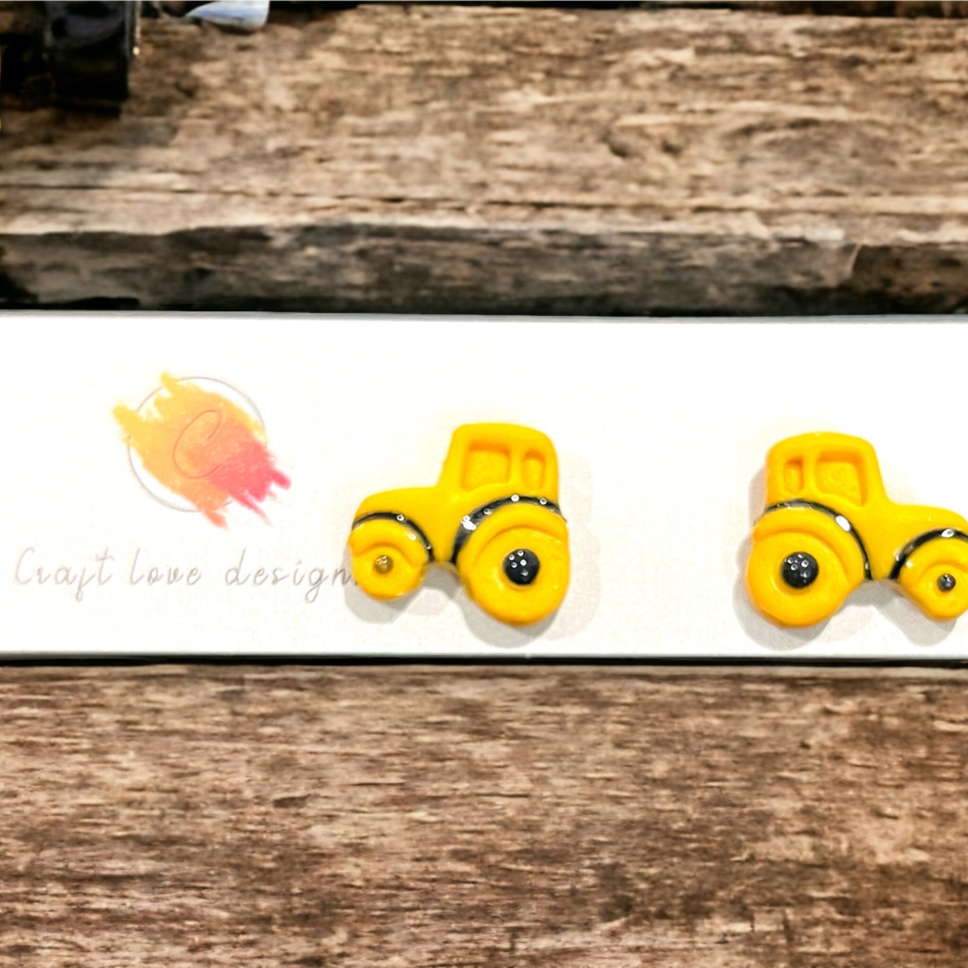Cute yellow tractor stud earrings displayed against a wooden backdrop, perfect for farm-themed or playful accessory lovers.
