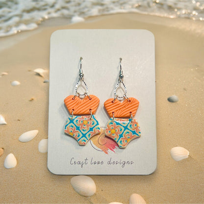 Close-up of playful polymer clay earrings with swimsuit shapes, featuring orange tops and patterned bottoms, perfect for beach vibes.