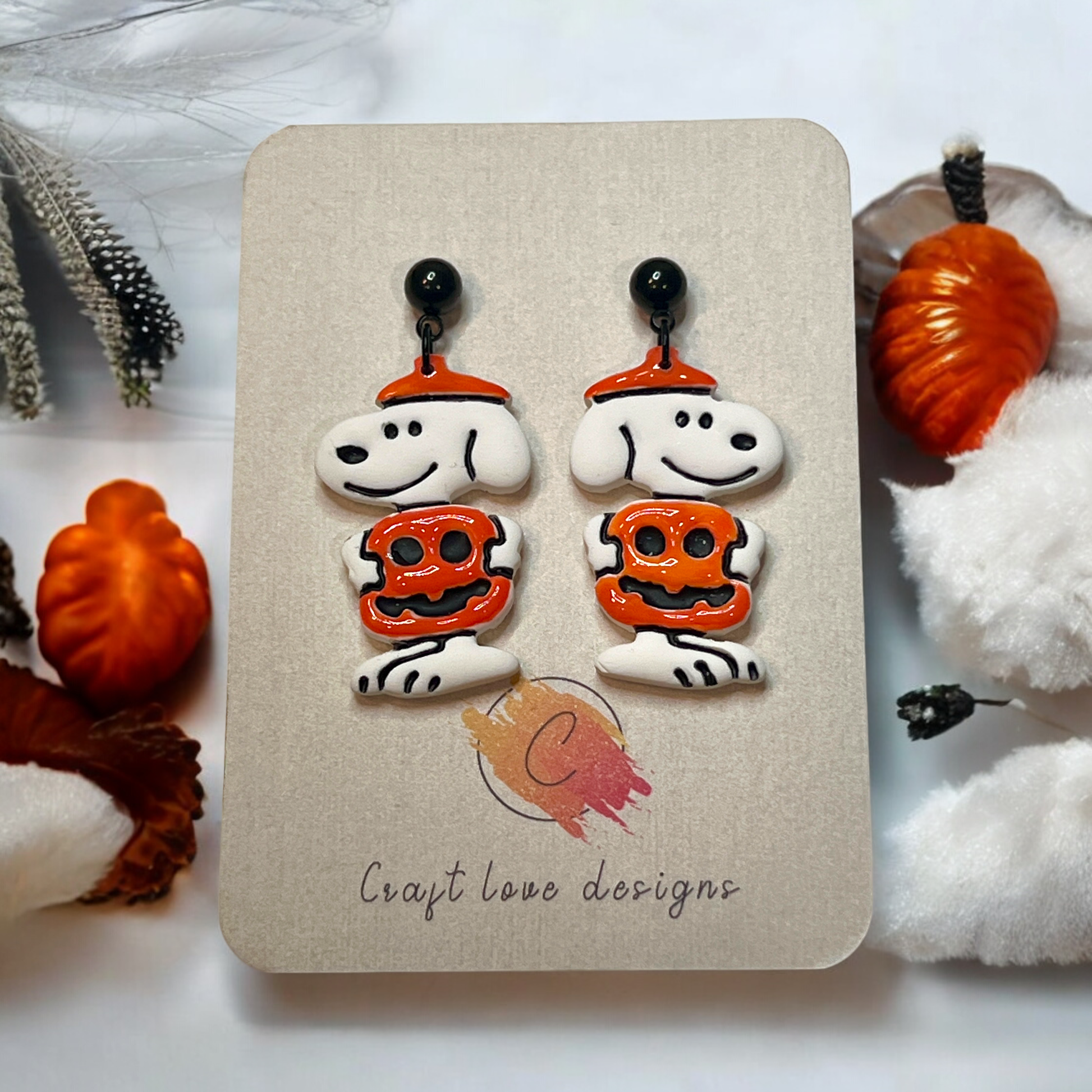 Cute polymer clay earrings featuring a white dog wearing an orange pumpkin costume and hat, perfect for fall and Halloween outfits.