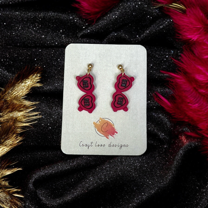 Red Heart Sunglasses-themed drop earrings displayed on a Craft Love Designs card, set against a black and gold sparkling fabric background.
