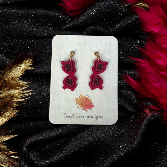 Red Heart Sunglasses-themed drop earrings displayed on a Craft Love Designs card, set against a black and gold sparkling fabric background.