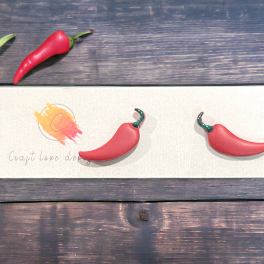 A close-up view of the Red Hot Chili Pepper stud earrings, featuring vibrant red peppers with green tops, set on a rustic display.