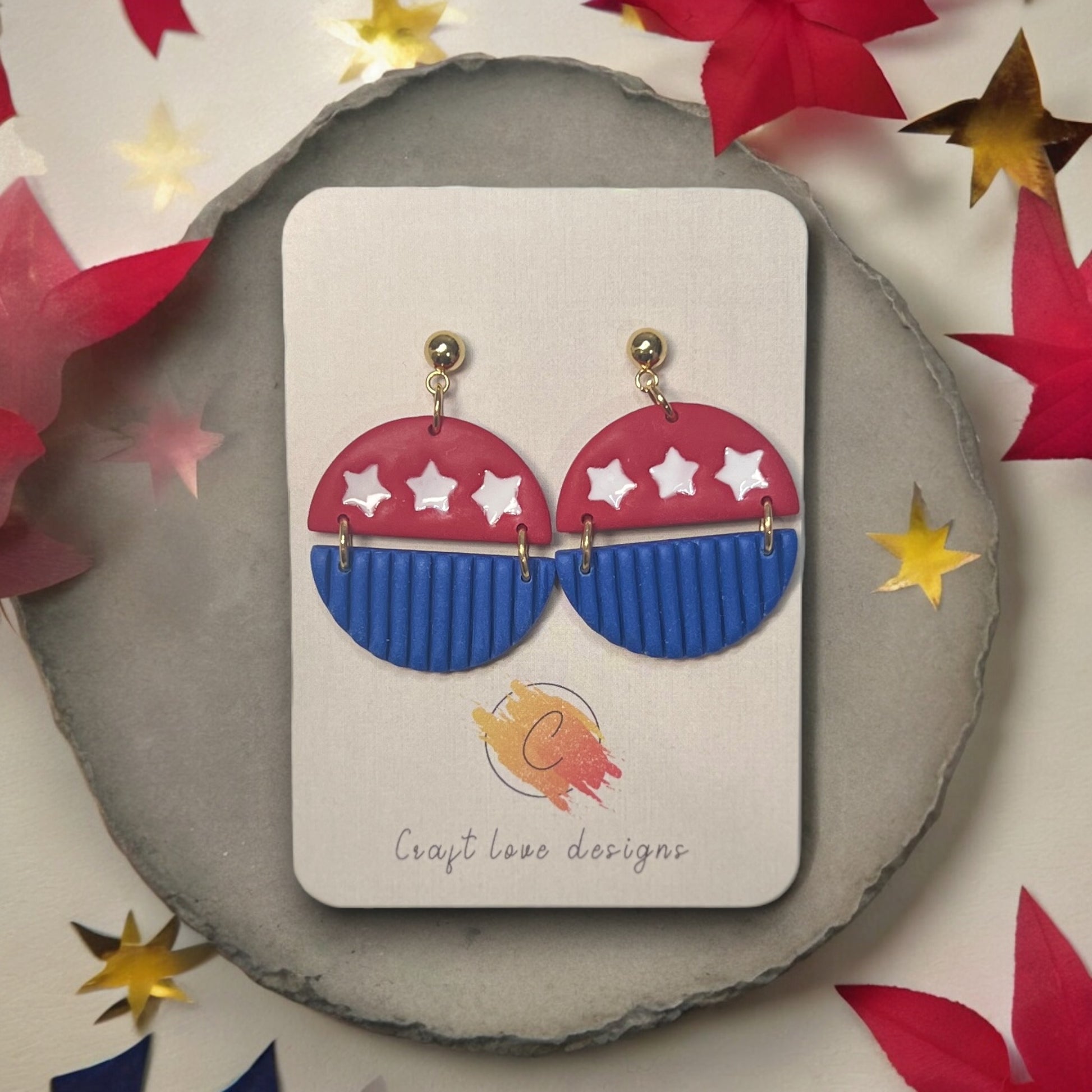 Handmade 4th of July polymer clay dangle earrings with red, white stars, and blue accents, displayed on a Craft Love Designs card.