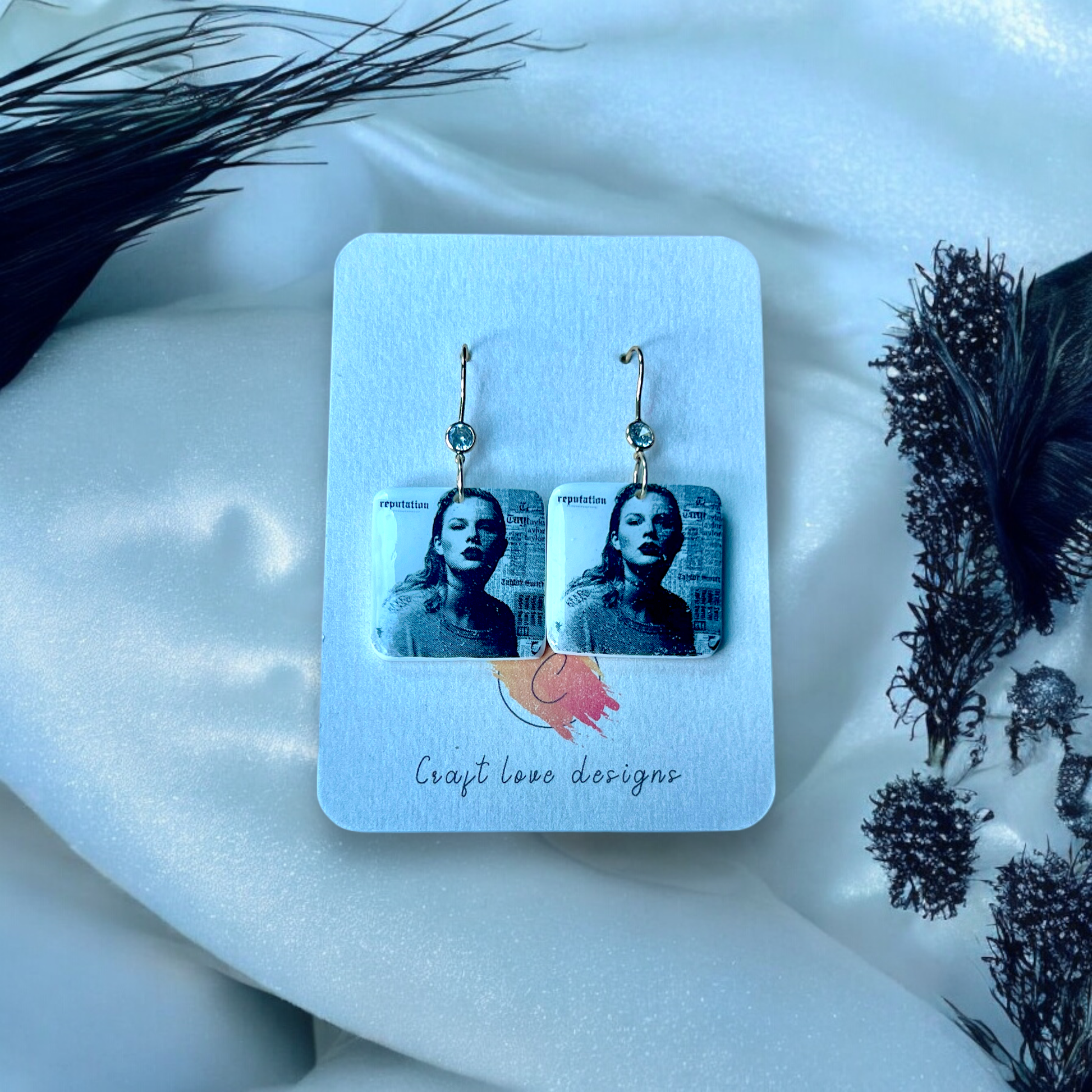 Square dangle earrings featuring a black-and-white portrait inspired by the Reputation album, set against a Craft Love Designs display card.
