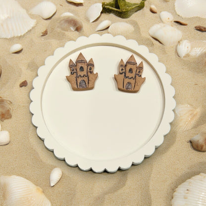 Beach-inspired sandcastle earrings displayed on a round white tray, surrounded by seashells on sandy beach decor.