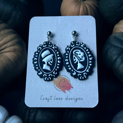  Black and white skeleton cameo earrings on a Craft Love Designs display card, surrounded by pumpkins and set in a spooky, dim setting.
