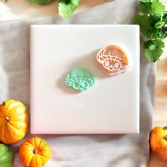 Finished clay cutout beside orange mushroom skull cutter on white tile with autumn decor
