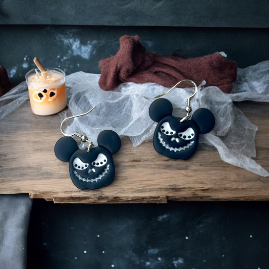  Black Mickey-shaped Halloween earrings featuring a spooky grin placed on a wooden table with cobweb decorations, candles, and eerie vibes. 