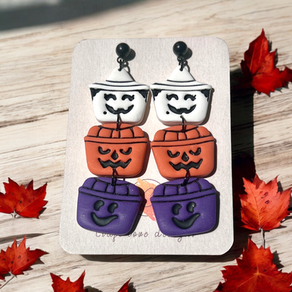 Halloween-themed stacked earrings featuring white ghost, orange pumpkin, and purple bucket charms on a Craft Love Designs display card. 