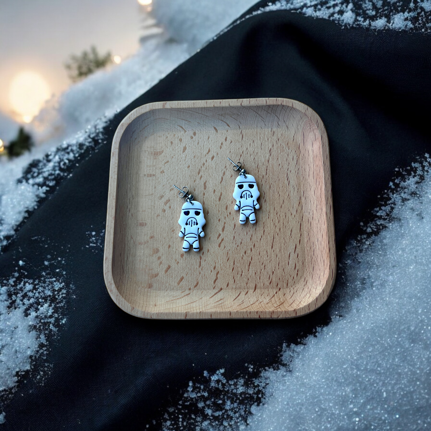 Stormtrooper earrings placed inside a wooden tray on a snowy surface, with soft ambient lighting and scattered snow creating a wintry atmosphere.
