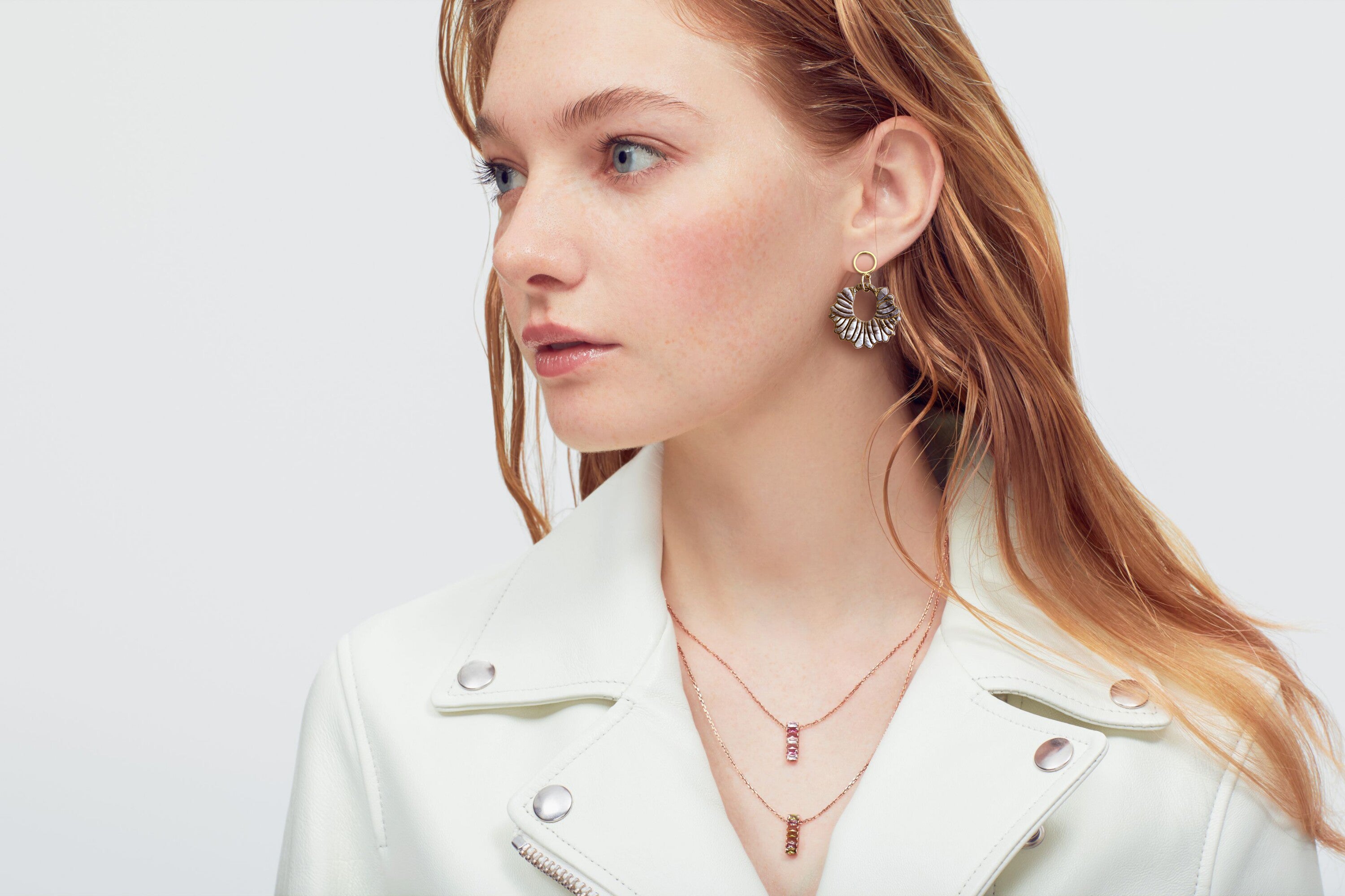  Side profile of a woman showcasing bold fan-shaped earrings and delicate layered necklaces, creating a trendy and modern accessory ensemble. 