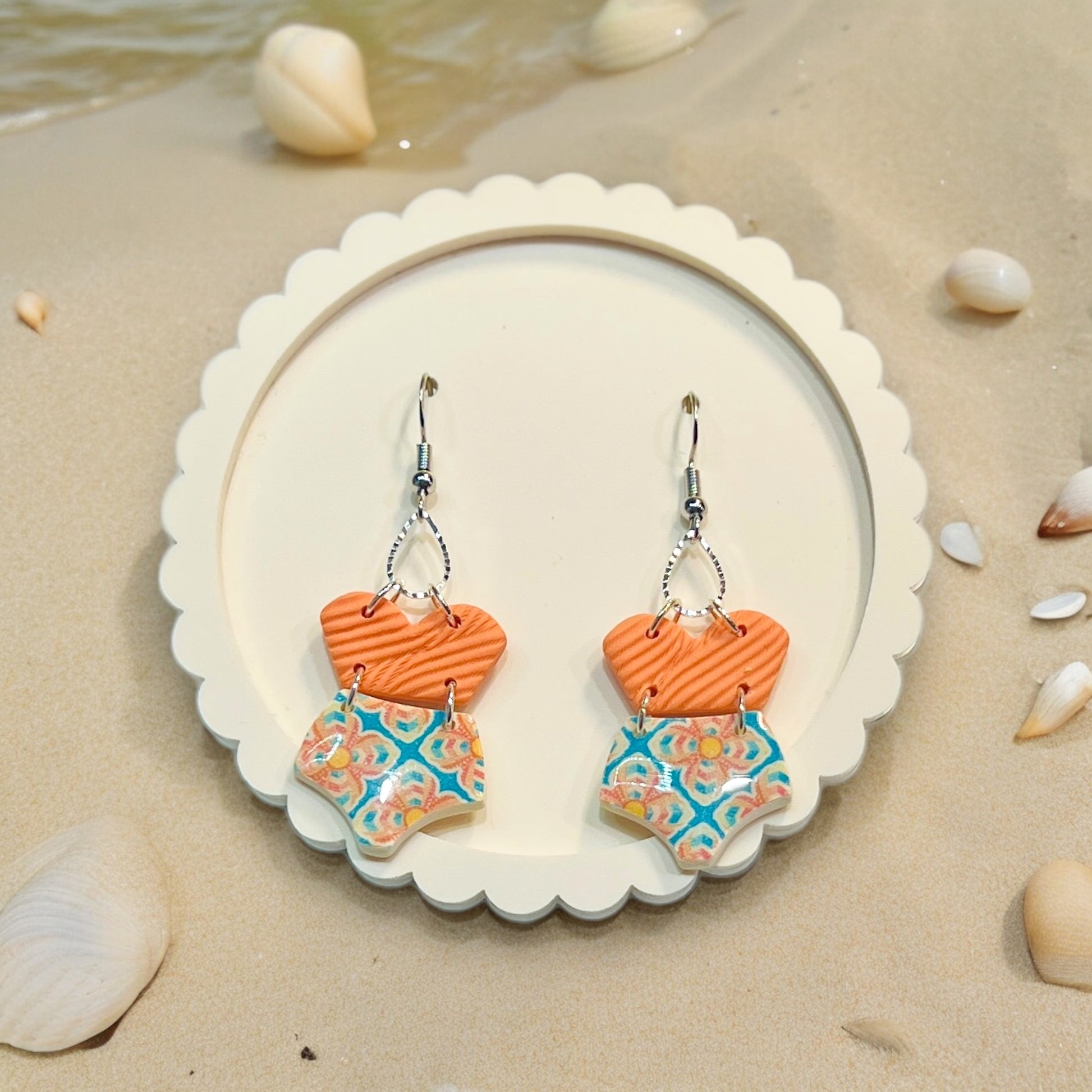 Summer-inspired polymer clay earrings shaped like swimsuits in orange and blue patterns, evoking a playful beachside charm. 