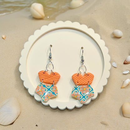 Summer-inspired polymer clay earrings shaped like swimsuits in orange and blue patterns, evoking a playful beachside charm. 