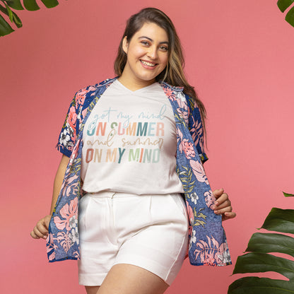 Woman wearing a summer quote t-shirt styled with a floral shirt and shorts, smiling against a pink background with tropical vibes. 