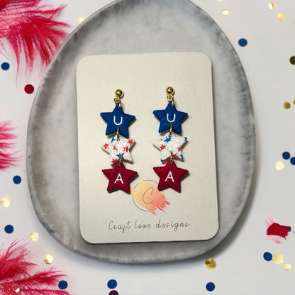 Handmade USA-themed star dangle earrings with red, white, and blue stars and gold hardware, displayed on a Craft Love Designs card.