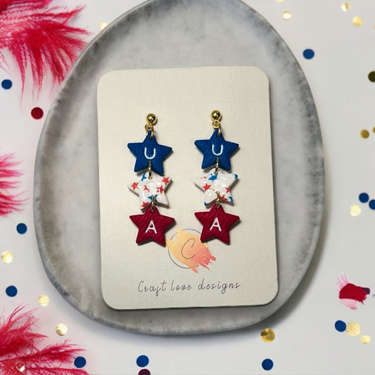 Handmade USA-themed star dangle earrings with red, white, and blue stars and gold hardware, displayed on a Craft Love Designs card.