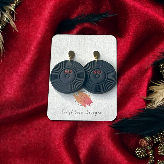 Black vinyl record-inspired dangle earrings with "Red" lettering, displayed on a Craft Love Designs card against a luxurious red fabric.