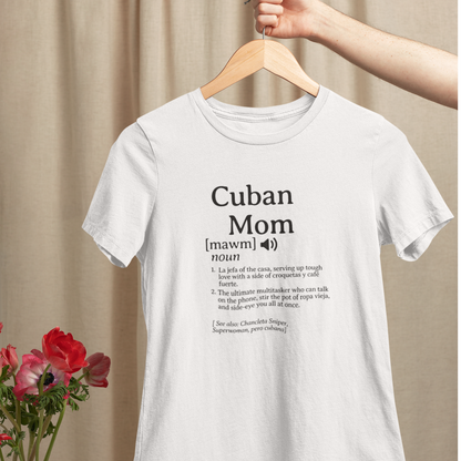 White Cuban Mom definition t-shirt hanging on a wooden hanger, displayed with nearby flowers against a soft neutral backdrop.background. 