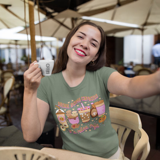Woman wearing green "Drink Some Cafecito y a Relax Mija" t-shirt with colorful coffee cup designs and playful text, perfect for coffee lovers.