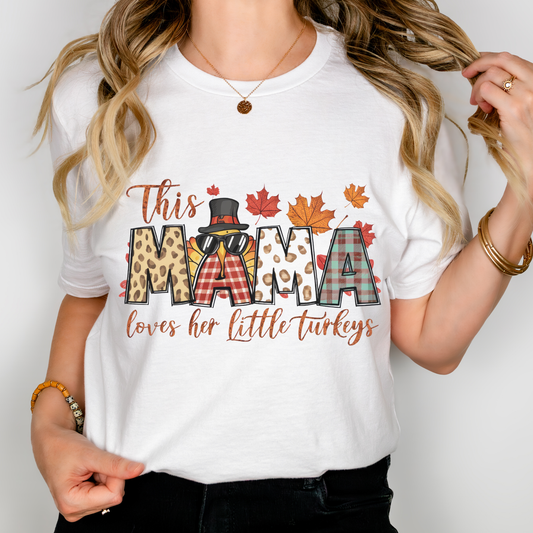 Woman wearing a white t-shirt with Thanksgiving-themed text "This Mama Loves Her Little Turkeys," styled with fall accents, plaid, and autumn leaves.