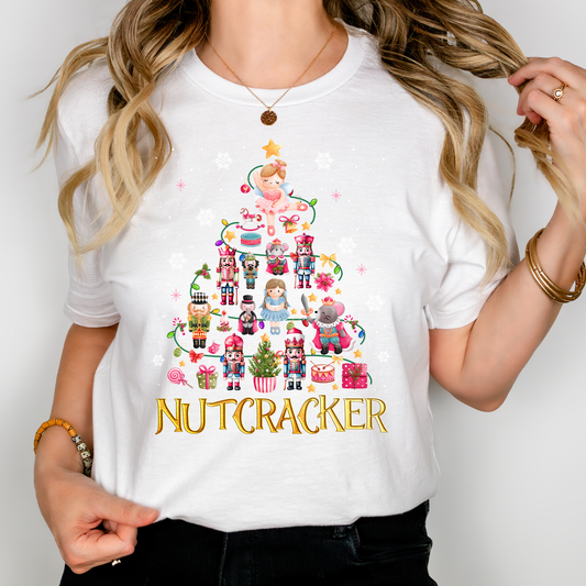 Woman wearing a white Nutcracker-themed Christmas t-shirt decorated with festive characters like Clara, nutcrackers, and a holiday tree.